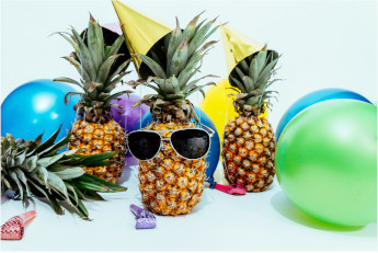 Ananas mit Sonnenbrillen und Luftballons im Hintergrund