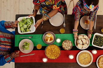 Drei Personen in bunten Gewändern sitzen an einem Tisch mit Essen.